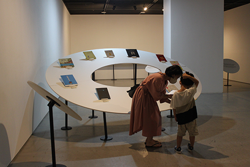 A mother recommending a book to her child (left) and exhibited books of “Our Stories” (right)