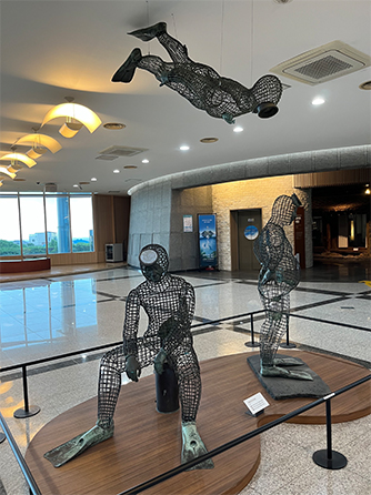 The exterior view of the Haenyeo Museum, displays in the lobby, and a photo of a haenyeo catching marine animals